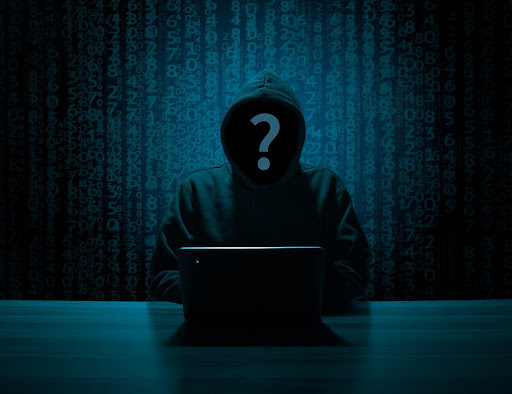 A person in a hoodie sits in front of a laptop in a dark room with a matrix of binary code in the background. Their face is obscured by a large question mark. The scene suggests anonymity and cybersecurity themes.