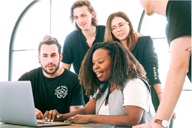 A diverse group of four professionals collaborates at a laptop, representing a managed services team working together to provide ongoing support, contrasting with the reactive approach of break/fix services.