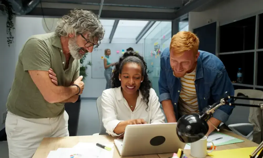 Three SMB leaders reading about I.T. outsourcing cost savings on a laptop