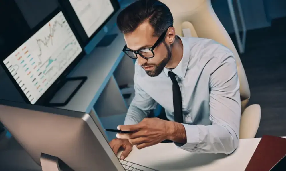 Top view of confident young man in shirt and tie using phone while staying late in the office.